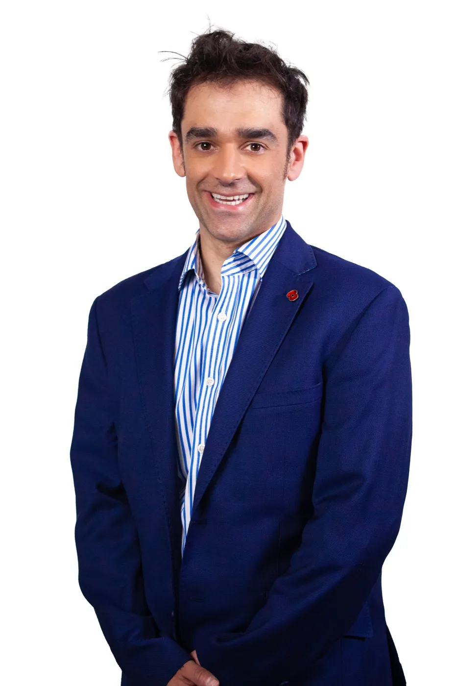 Studio headshot of Dr Kishan Rees in a navy blazer and blue striped shirt, smiling to camera on a white background.
