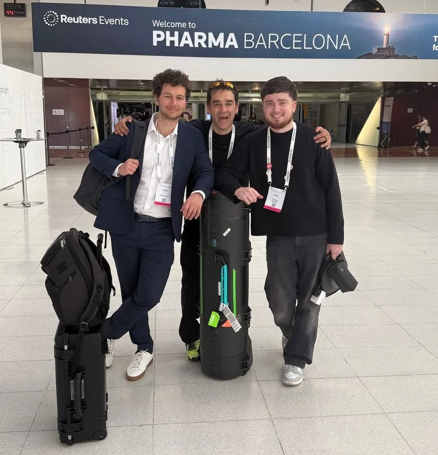 Kishan Rees, arms around Cormac and Sacit, with their filming cases under the Reuters Pharma Barcelona sign.