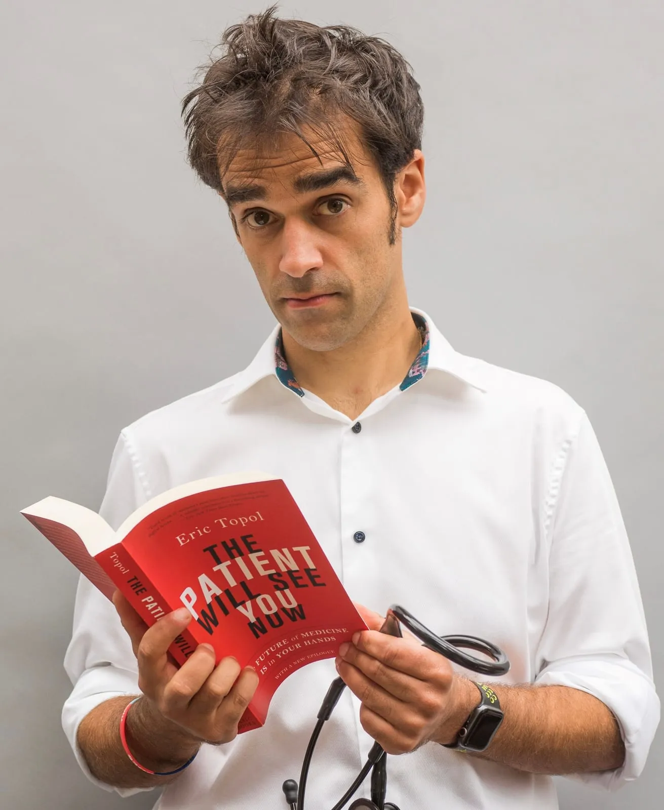 Kishan Rees, in a white shirt with a stethoscope, holding Eric Topol's book The Patient Will See You Now.